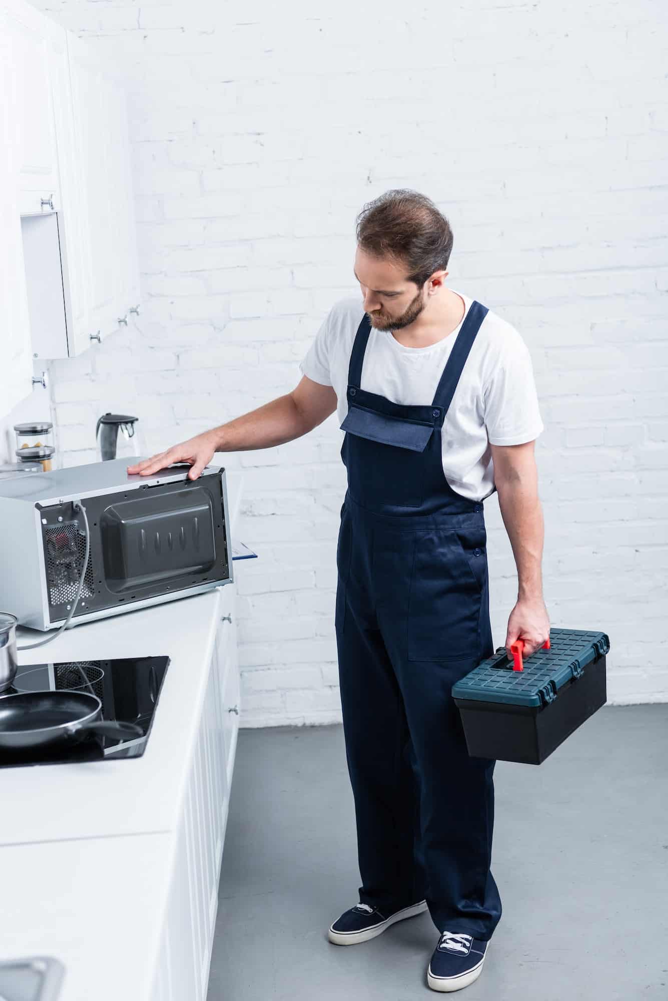 high angle view of adult handyman with toolbox checking microwave oven in kitchen