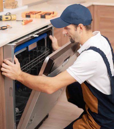 A man or service worker in special clothing installs, disassembles or performs maintenance of a dishwasher built into the kitchen furniture